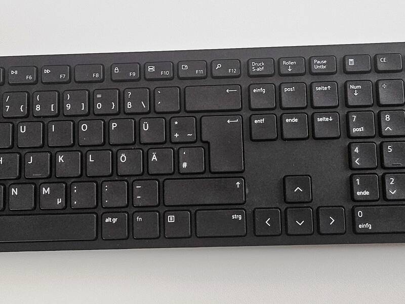 Das Bild zeigt eine schwarze Computertastatur neben einer kabellosen Maus auf einer weißen Oberfläche.