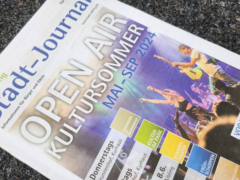 Auf dem Bild ist eine geöffnete Ausgabe des "Stadt-Journals" zu sehen, welche Werbung für eine Open-Air-Kulturveranstaltungsreihe im Sommer mit dem Titel "OPEN AIR KULTURSOMMER" macht.